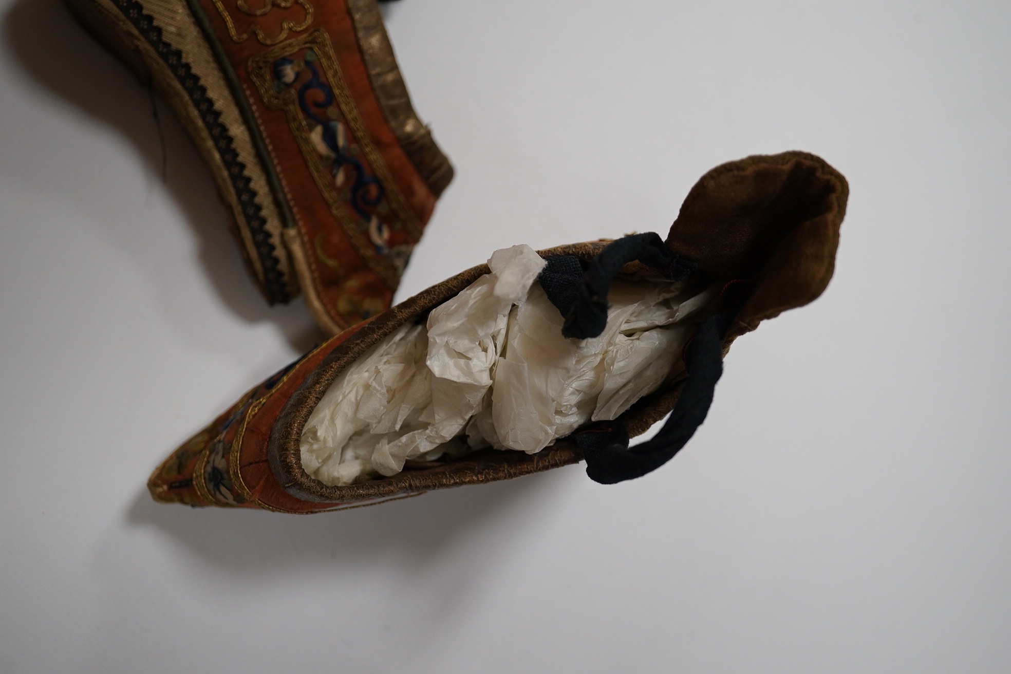 A pair of Chinese silk and gold thread embroidered ladies shoes, with leather binding around the top and gold brocade platform heels with fine blue braiding, 12cm long. Condition - good for age and use